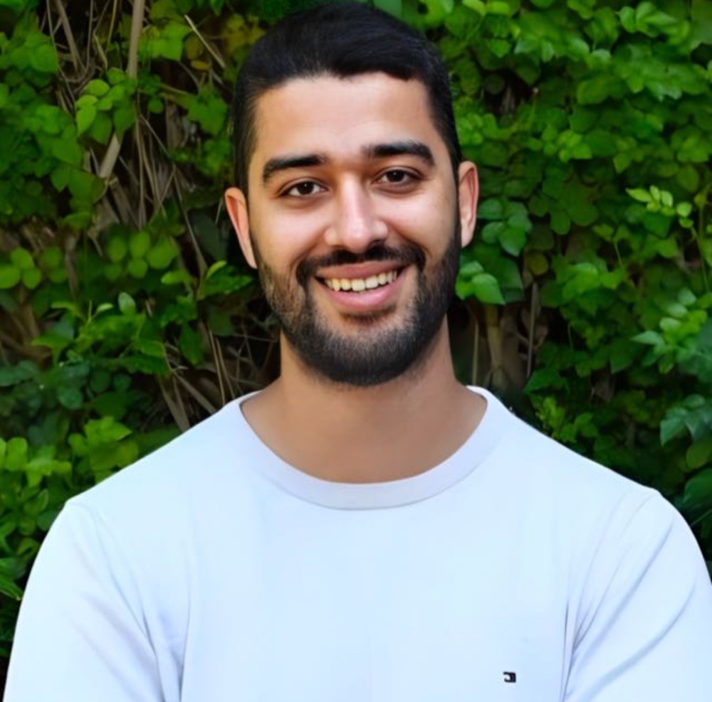 Taieb Bendai smiling outdoors in front of green foliage.